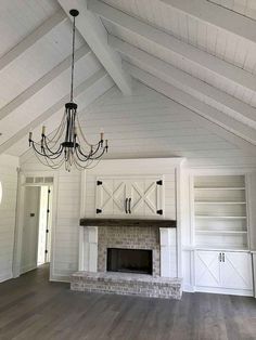 an empty living room with a fireplace and chandelier hanging from the vaulted ceiling