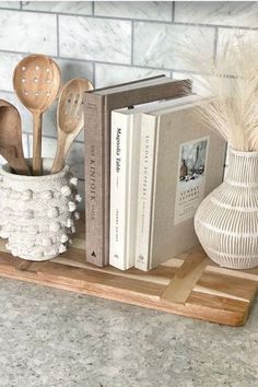 some books and spoons are on a shelf next to a vase with feathers in it