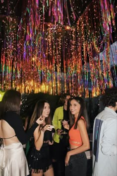 two women standing next to each other in front of a chandelier filled with multicolored lights