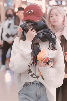 a woman is walking through an airport with her scarf around her neck and hat over her head