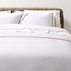 a bed with white sheets and brown trimmings on the headboard is shown