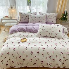 a bed covered in white and purple sheets next to a window with flowers on it