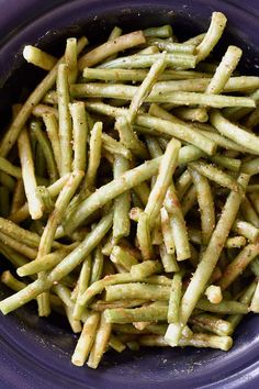 a purple bowl filled with green beans on top of a table