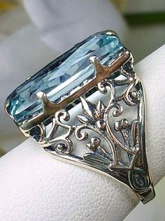 Sky Blue Aquamarine Ring Baguette Design#32 Introducing the Baguette D32, a stunning piece of wearable art that pays homage to the opulent Victorian era. Crafted with meticulous attention to detail, this exquisite filigree Antique reproduction in sterling silver is sure to captivate anyone with a love for vintage-inspired jewelry. At its center, lies a flawless 7ct sky blue gemstone, radiating a dazzling hue that catches the light with every movement. The baguette rectangle-cut gemstone measures Elegant Oval Crafted Jewelry, Elegant Formal Rings With Jewels, Classic Blue Jewelry For Evening, Blue Art Deco Jewelry For Evening, Elegant Engraved Blue Jewelry, Vintage Blue Rectangular Rings, Rectangular Blue Ring For Wedding, Blue Evening Rings, Elegant Blue Jewelry With Intricate Design