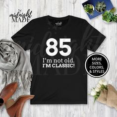 "Looking for a unique funny 85 year old gift? This Midnight Made® 85 Not Old Classic T-shirt Tee is sure to delight! This 85th Birthday shirt is a perfect 85th Birthday, Bday, or Senior Elderly Adult Theme Party gift for an 85 year old. This under 30 dollars novelty graphic 85th Birthday Tshirt Top is also a great present or gift idea for Christmas, Hanukkah, or other holidays. T-SHIRT DETAILS:  Made to order and individually printed directly on the item (NOT an iron-on decal) on a comfortable, high quality, 100% cotton (fiber content may vary depending on color) short-sleeved T-Shirt. The back is blank, unless pictured otherwise. Multiple colors (light designs on dark shirts, dark designs on light shirts, and high-contrast full-color designs print well on either dark or light shirts) and Funny 70th Birthday, Old Tshirt, 95th Birthday, Dark Designs, 85th Birthday, Idea For Christmas, Bday Gift, 100th Birthday, Old Shirts