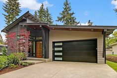 a house with a large garage in front of it and landscaping around the driveway area