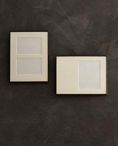 two white frames on a black wall one is empty and the other has no image