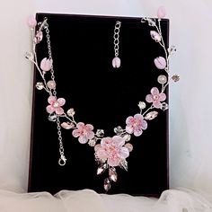 a necklace with pink flowers and crystal beads on a black display stand in front of a white background