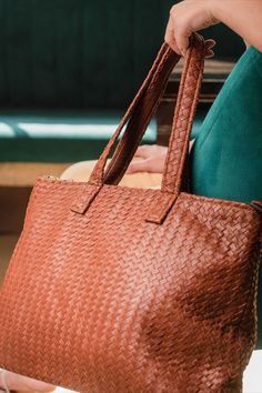 a woman is holding a brown woven bag