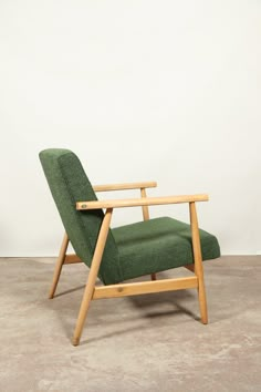 a green chair sitting on top of a cement floor next to a wooden framed wall