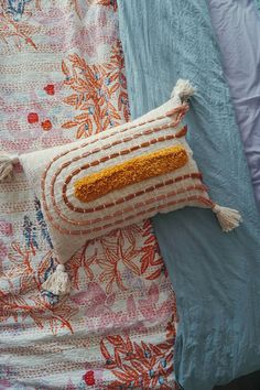 an orange and white pillow sitting on top of a bed next to a blue comforter