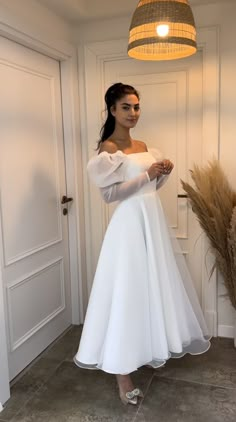 a woman wearing a white dress standing in front of a door with her hands on her hips