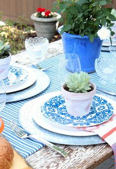 an outdoor table set with plates, cups and vases filled with succulents