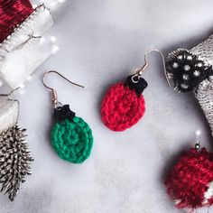 three crocheted christmas ornaments are displayed on a white surface, one is red and the other is green