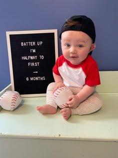 a baby sitting on top of a table holding a baseball