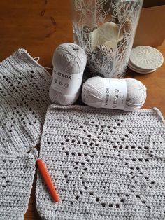 a crocheted table cloth and two balls of yarn next to a glass vase