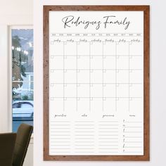 a family calendar hangs on the wall next to a chair and table in front of a window