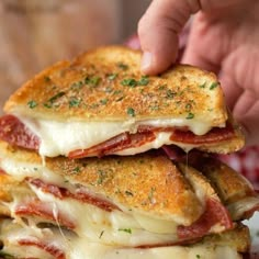 a stack of sandwiches with meat and cheese on them being held by someone's hand