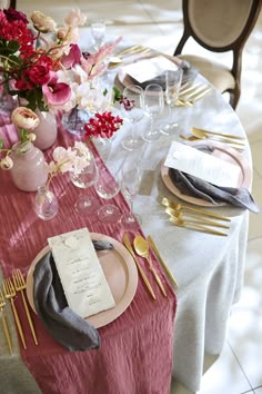 the table is set with silverware and pink flowers