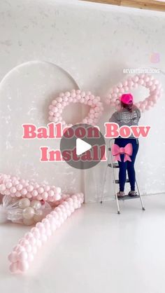 a person standing on a ladder in front of a balloon wall with pink balls and bows