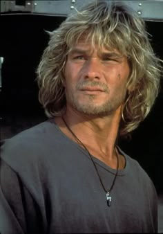 a man with long blonde hair wearing a black t - shirt and looking off to the side