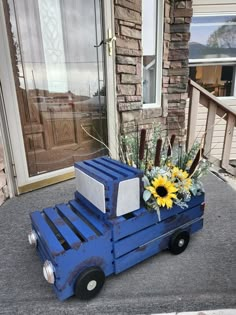 a blue truck with sunflowers and other flowers in it sitting on the sidewalk