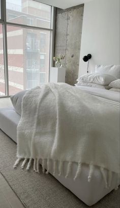 a bed with white linens and pillows in a bedroom next to a large window