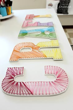 the letters are made out of string and have different colors on them, including pink, yellow, green, blue