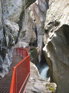 a red fence is in between two large rocks and a narrow path that leads to a waterfall