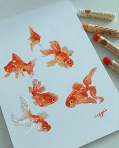 four goldfish drawn on paper with crayons next to them