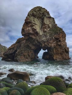 a rock formation in the ocean with green moss growing on it's rocks and water