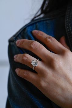 a woman's hand with a diamond ring on her left hand and a blue jean jacket in the background