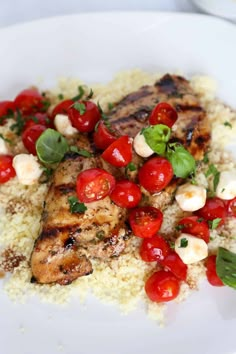 a white plate topped with meat and rice covered in cherry tomatoes, garnished with basil