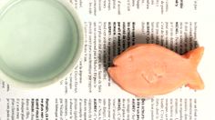 an orange fish shaped cookie next to a green cup on top of a book page