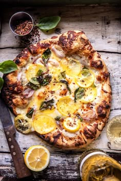 a pizza sitting on top of a wooden table next to some lemons and herbs