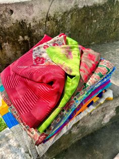 a pile of colorful cloths sitting on top of a cement bench next to a wall