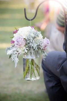 a mason jar filled with flowers hanging from a metal hook on a pole in the grass