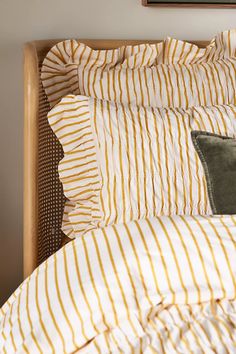 a bed with yellow and white striped sheets, pillows and pillow cases on top of it