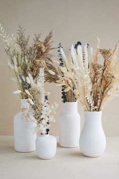 three white vases with dried plants in them