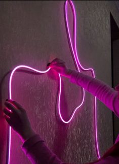 a person holding a neon light up in front of a wall with an object on it