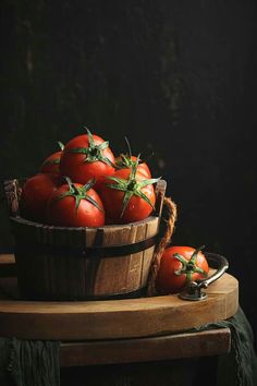 a wooden basket filled with lots of ripe tomatoes on top of a table next to a knife