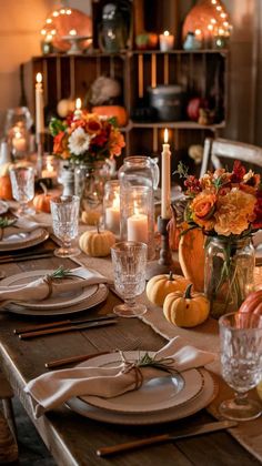 a table set for thanksgiving dinner with candles and pumpkins in the center, surrounded by other decorations