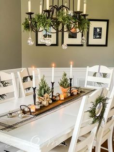 a dining room table decorated for christmas with candles and greenery on the centerpiece