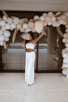 a woman standing in front of a bunch of balloons with palm leaves on top of it