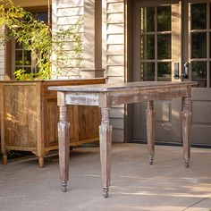 a wooden table sitting on top of a patio next to a building with windows and doors