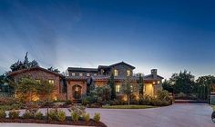 a large house with lots of trees and bushes in front of it at night time