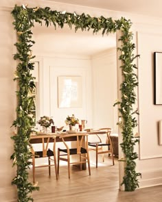 a dining room with a table and chairs covered in greenery next to a mirror