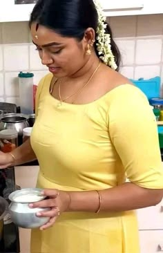 a woman in a yellow dress is holding a bowl and looking at something on the counter