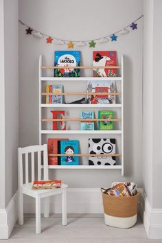 a white book shelf filled with books in a child's playroom next to a chair