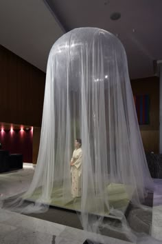 a woman standing in front of a white tent covered with mosquito netting on the floor